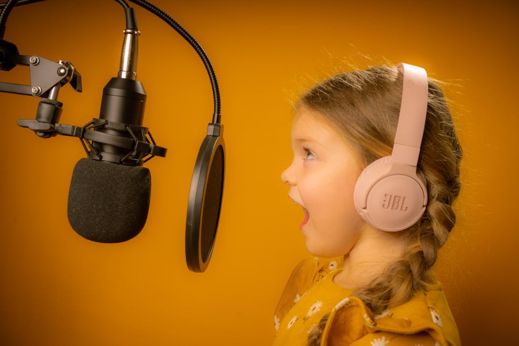 A Girl in Yellow Shirt Singing while Wearing Pink Headphones